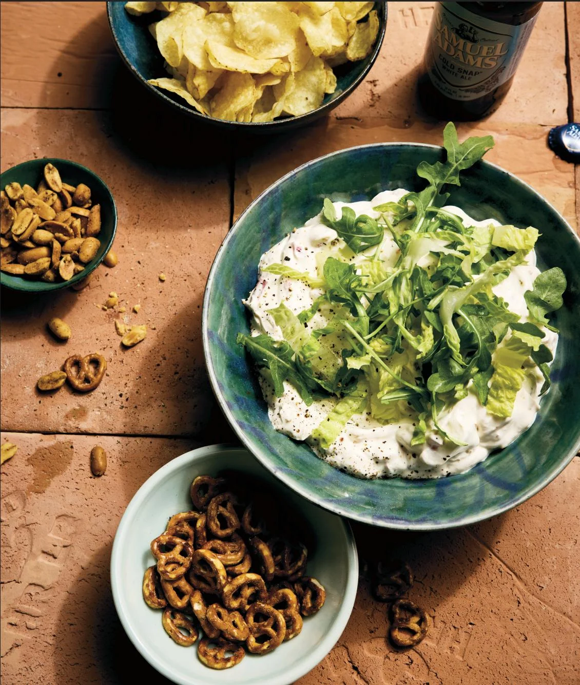 A spread of Teodora's summer tasting bites — a creamy dip topped with fresh greens, kettle chips, pretzels, spiced peanuts, and a Samuel Adams beer.
